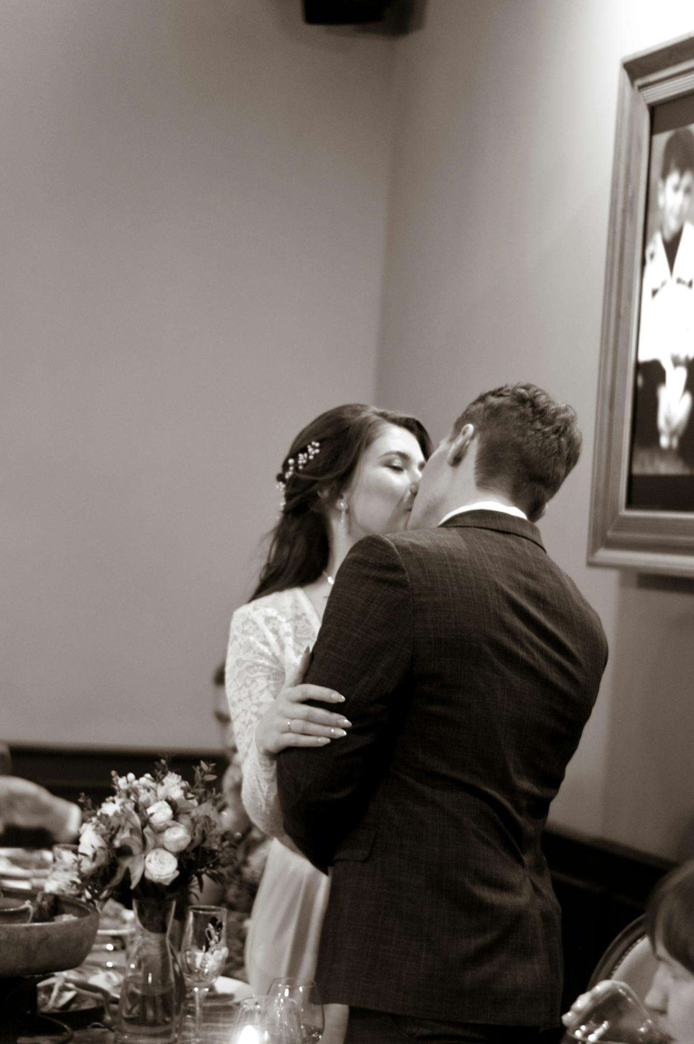 Emotional moment of a couple kissing at their wedding reception in black and white.